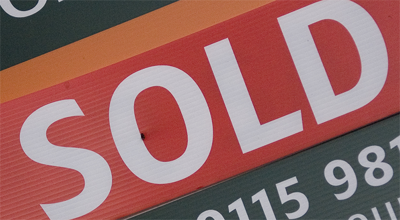 This image is photograph of a woman holding a “sold” sign.