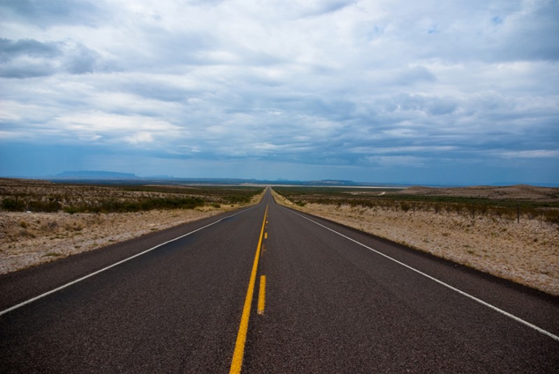 A long isolated double-lane road banked by barren land on both sides.