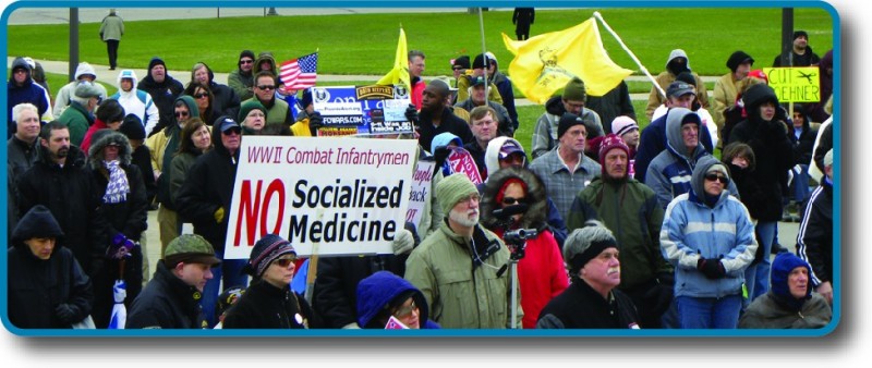 An image of a crowd of people holding signs and flags. One sign reads 